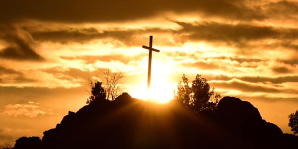 Una cruz en lo alto de una montaña con una puesta de sol de color rojo dorado al fondo